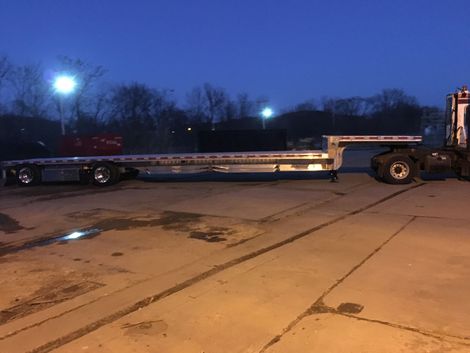 Flatbed trailer attached to a semi-truck on a concrete surface at dusk.