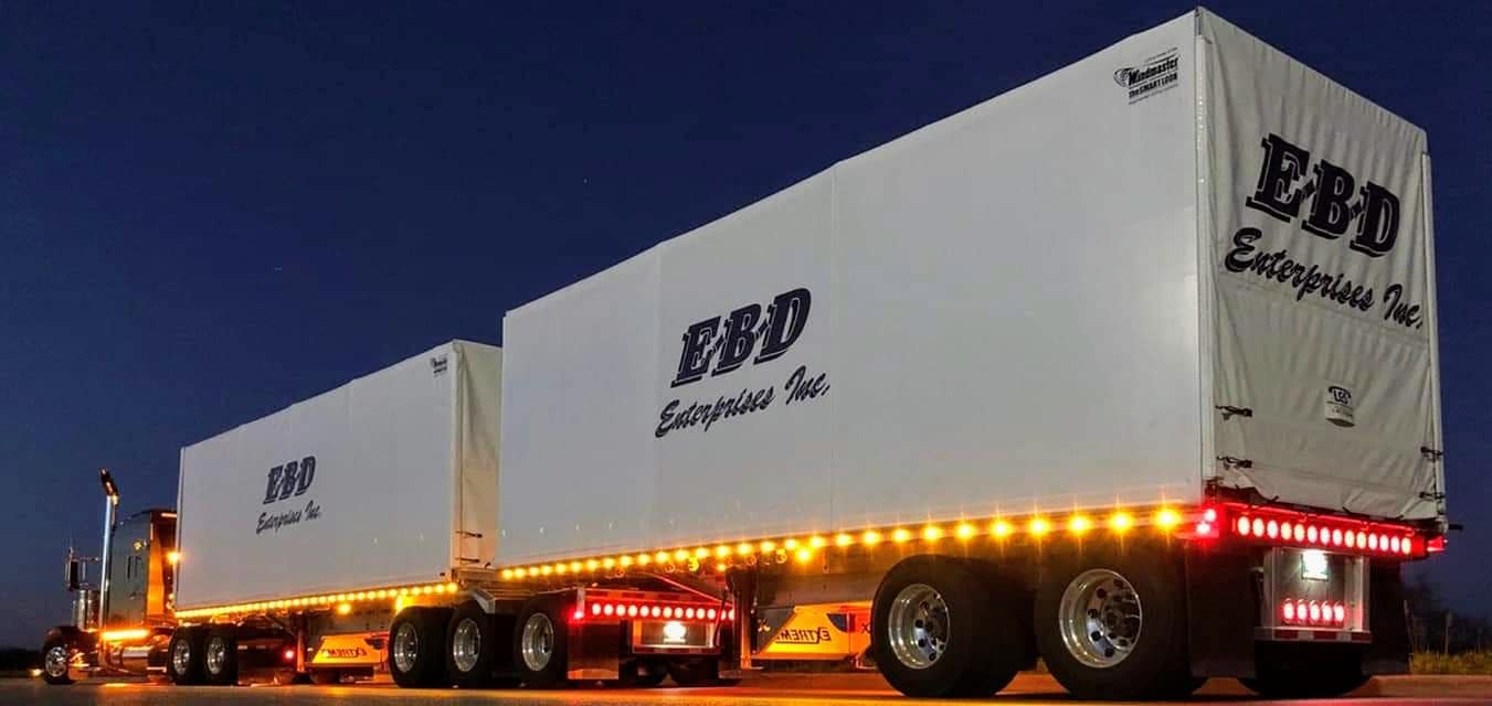 A semi-truck with two connected trailers; illuminated with lights; logo 