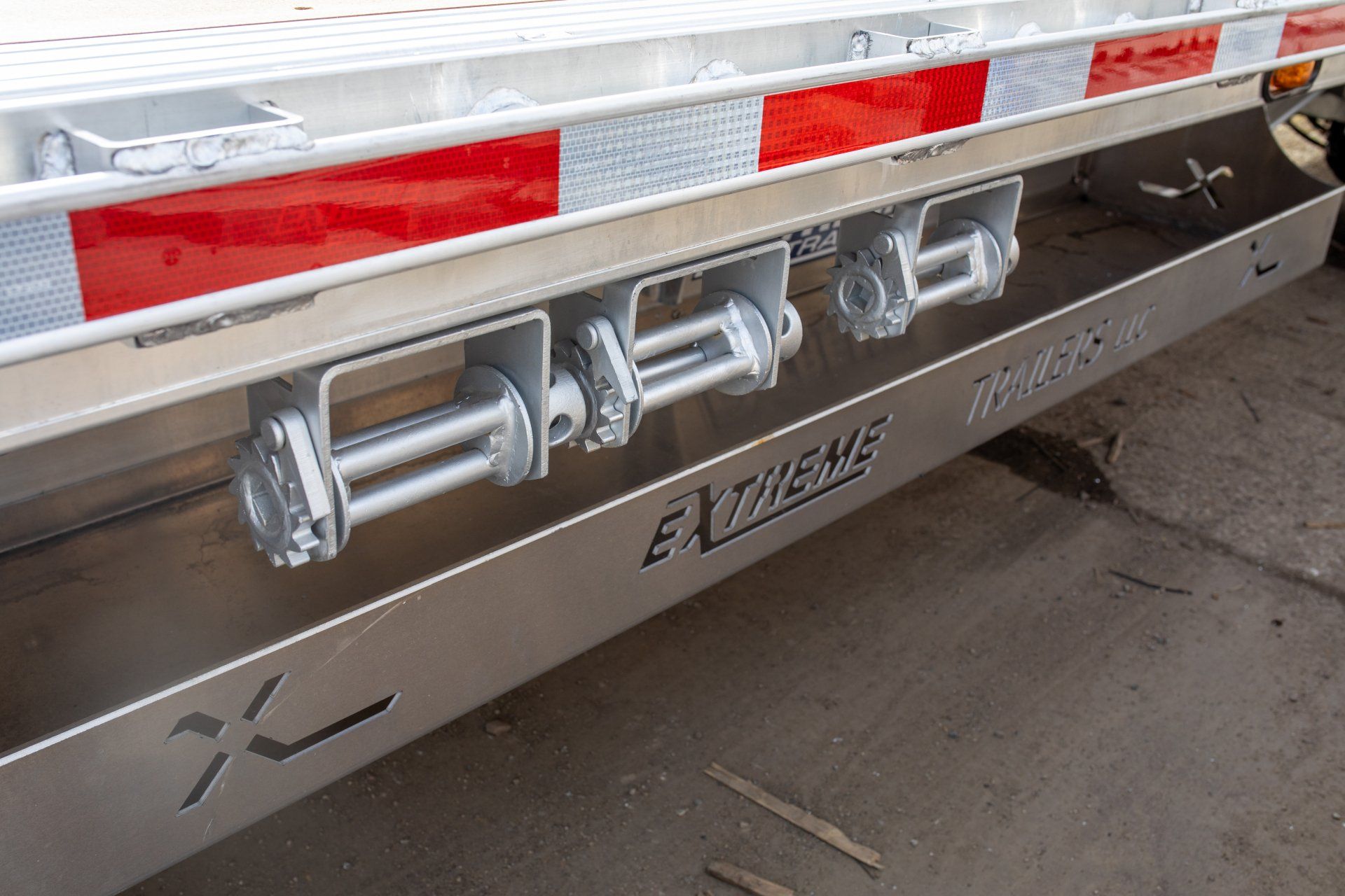 Side view of a flatbed trailer with three silver winches mounted on a metallic panel. Red and white reflective tape is above.