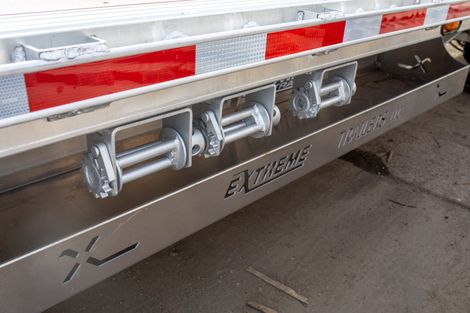 Side view of a flatbed trailer with three silver winches mounted on a metallic panel. Red and white reflective tape is above.