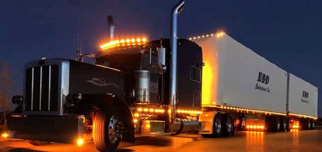 Black semi-truck with orange lights at night; white trailer with 