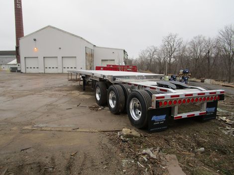 Flatbed semi-trailer parked in a lot, with a factory building in the background. Cloudy day.
