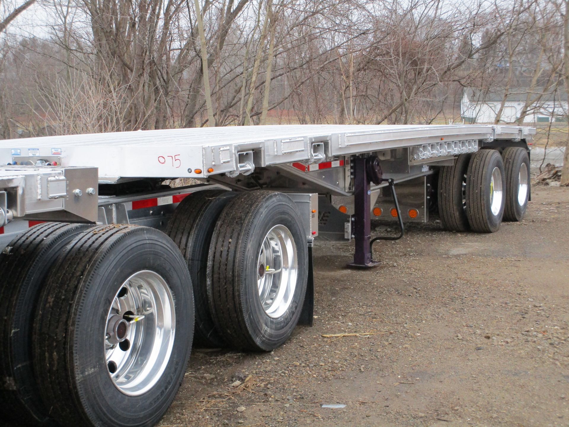 Flatbed trailer with dual wheels, parked on gravel.