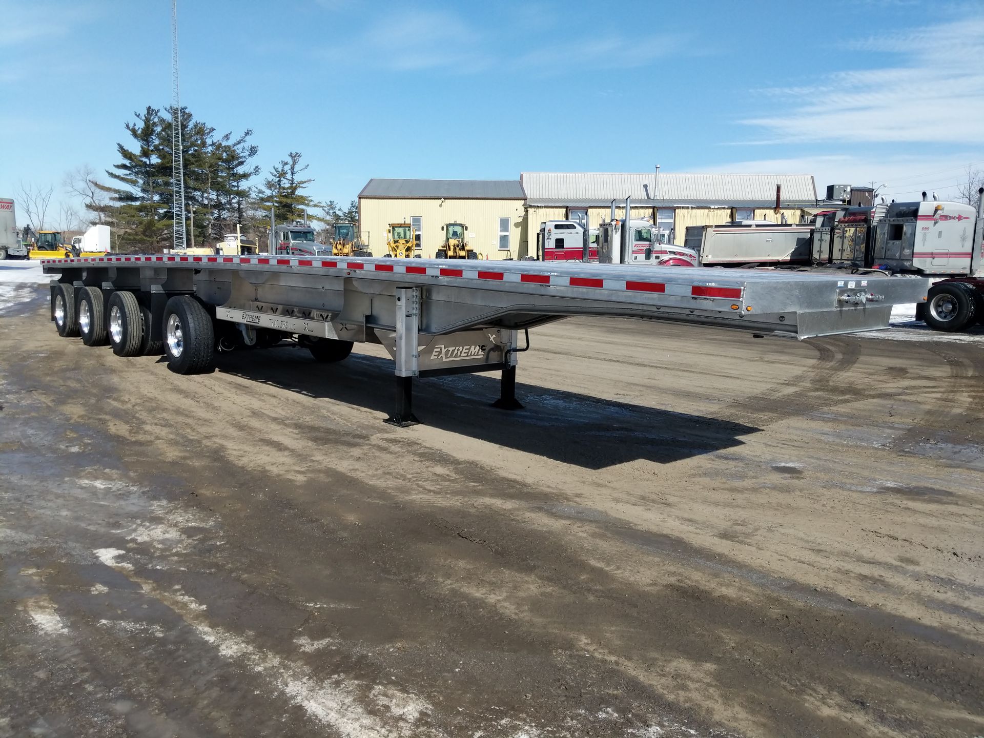 Flatbed trailer parked outdoors on a snow-covered surface under a bright sky.