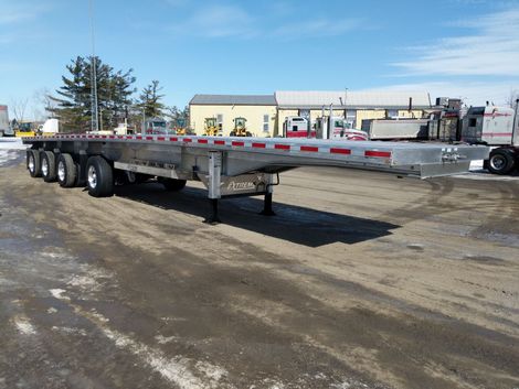 Flatbed trailer parked outdoors on a snow-covered surface under a bright sky.