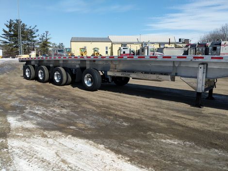 Flatbed trailer with multiple axles parked outdoors on a sunny day.