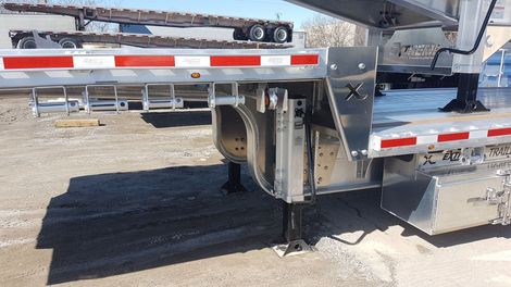A car hauler trailer with aluminum frame, red/white reflective tape, and a jack support system on gravel.