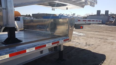 A flatbed trailer with reflective stripes and a metal panel. Exterior setting, daytime.