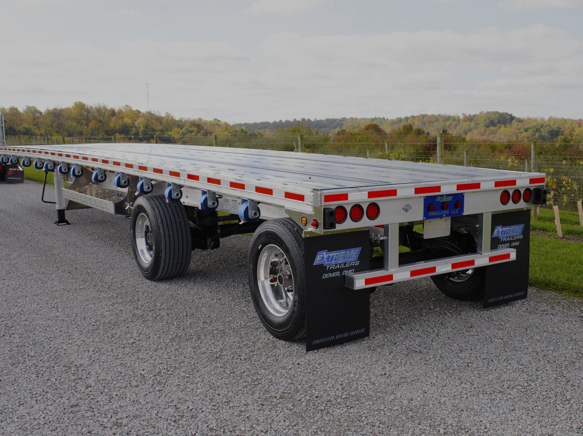 Flatbed trailer parked on gravel, with tires and red taillights visible.