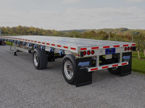 Flatbed trailer parked on gravel, with tires and red taillights visible.