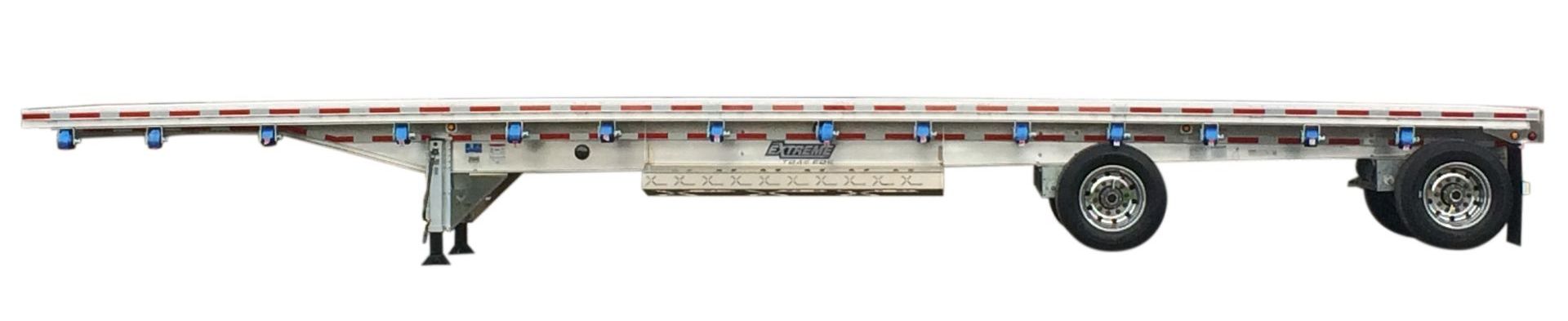 A silver flatbed trailer with a white background. It has wheels and supports, ready for hauling cargo.