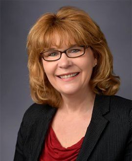 Woman with red hair and glasses smiling in a red blouse and black suit jacket.