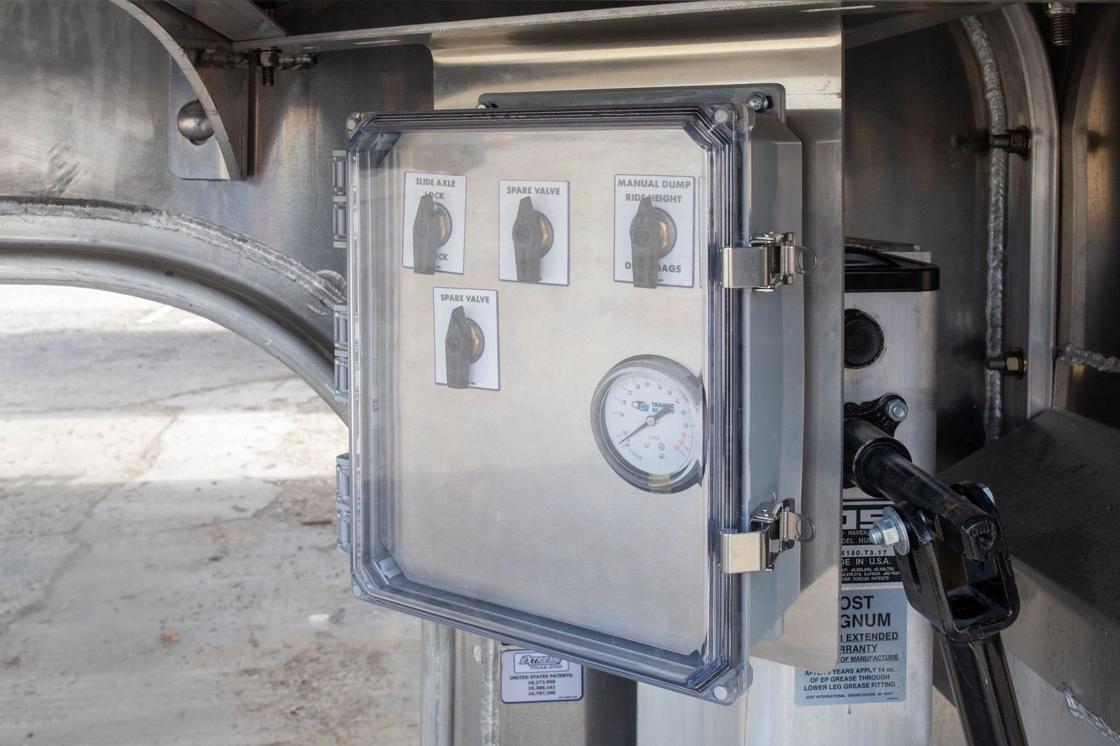 Metal control panel with clear cover and gauge. Displays diagrams and readings. Mounted on industrial equipment.