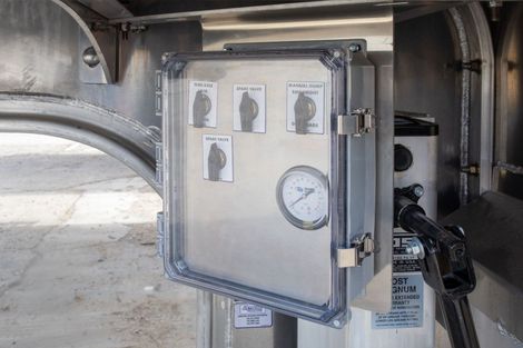 Metal control panel with clear cover and gauge. Displays diagrams and readings. Mounted on industrial equipment.