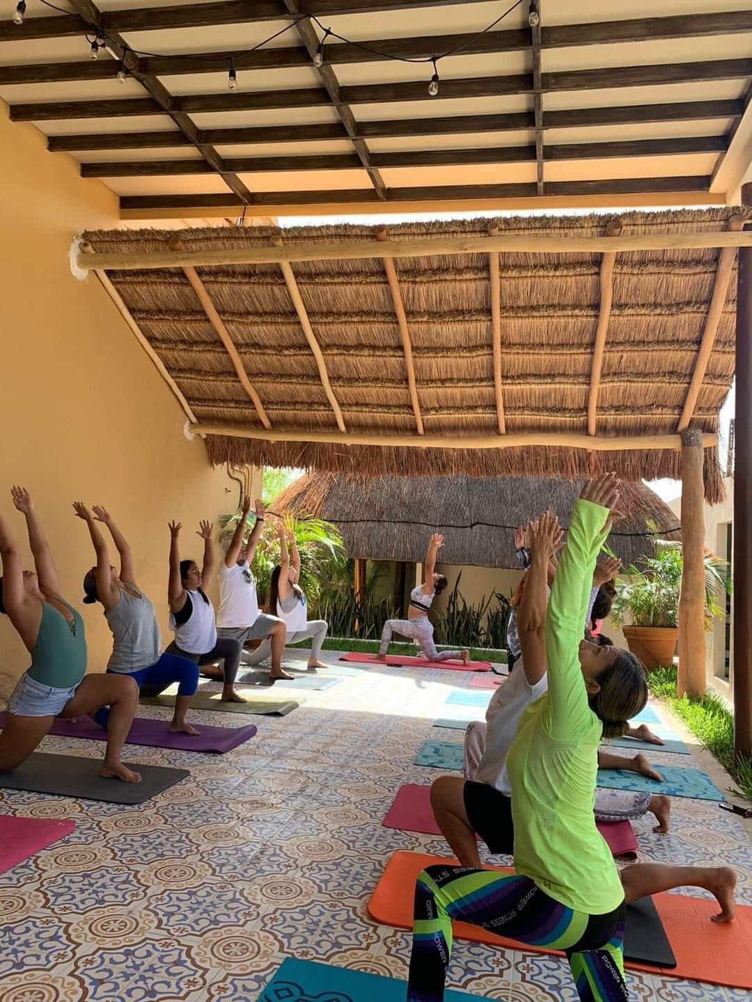 Un grupo de personas está haciendo yoga en una habitación bajo un techo de paja.