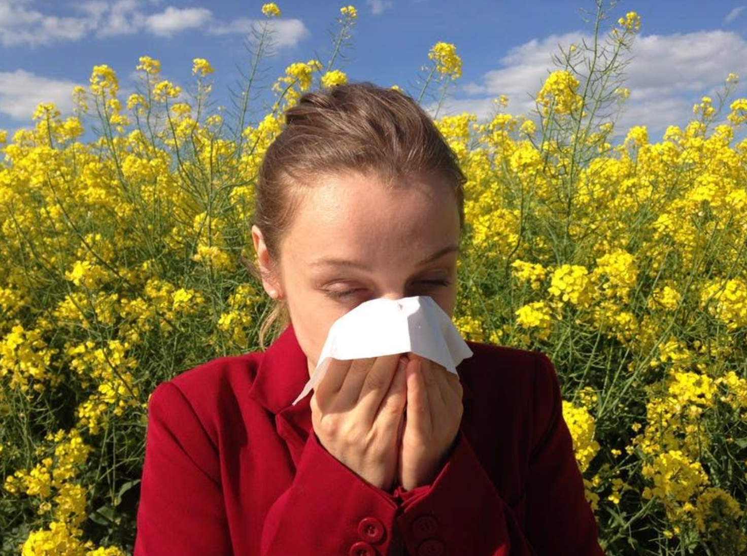 A woman is blowing her nose in front of a field of yellow flowers.