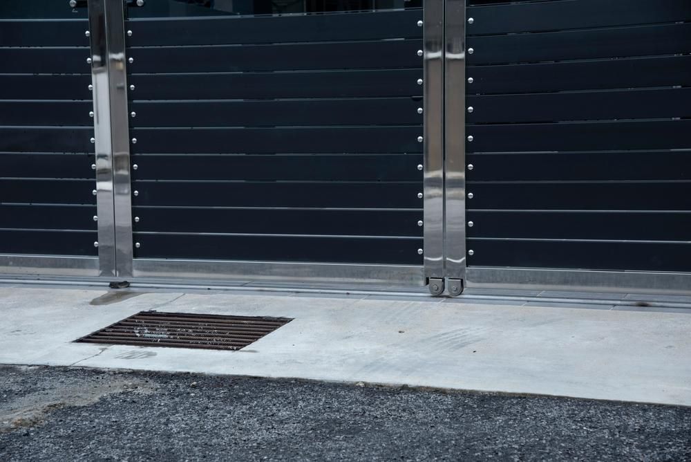 A Black Fence With Stainless Steel Posts And A Manhole Cover In Front Of It — Rabbo's Fencing Services In Noonamah, NT