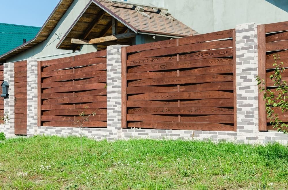 A Wooden Fence Is Surrounded By Brick Pillars In Front Of A House — Rabbo's Fencing Services In Howard Springs, NT