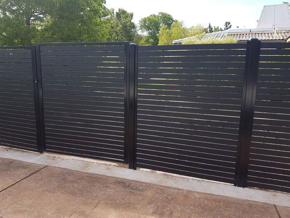 A Black Fence Is Sitting On Top Of A Concrete Driveway — Rabbo's Fencing Services In Pinelands, NT