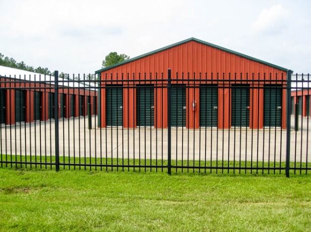 A Fence Surrounds A Storage Facility With A Red Building In The Background — Rabbo's Fencing Services In Pinelands, NT
