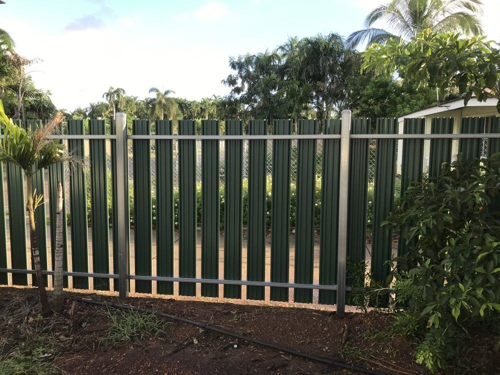 A Green Fence Is Surrounded By Trees And Bushes — Rabbo's Fencing Services In Pinelands, NT