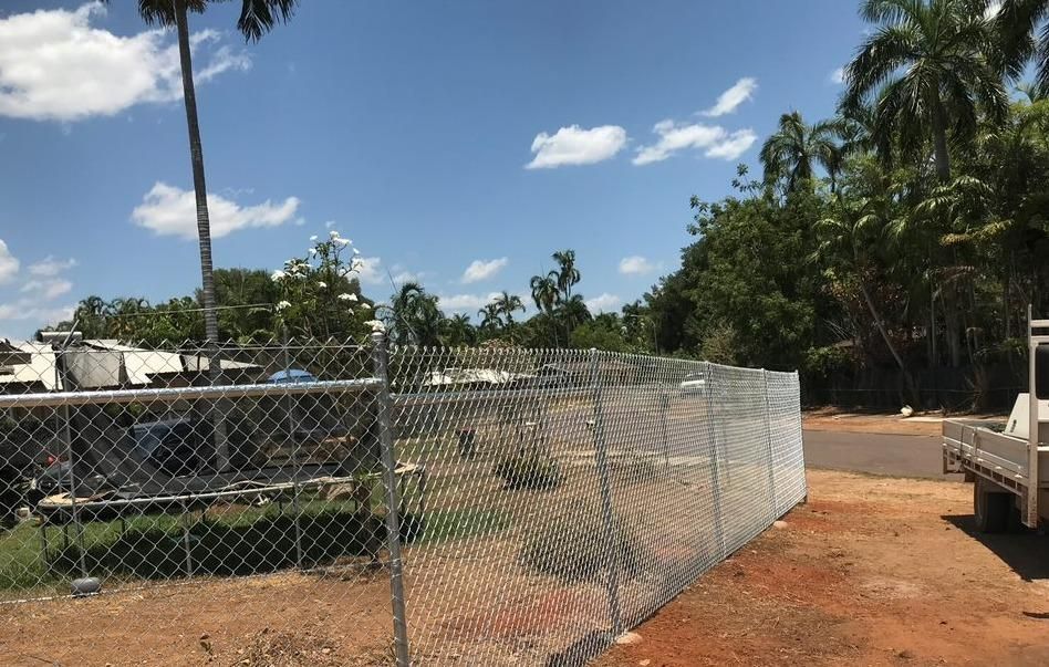 A Chain Link Fence Is Surrounding A Dirt Area With Trees In The Background — Rabbo's Fencing Services In Pinelands, NT