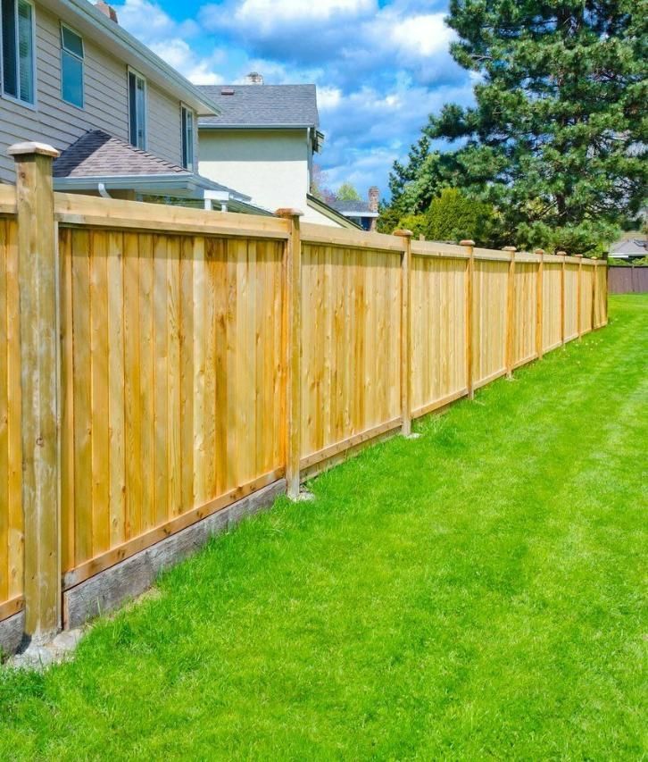 A Wooden Fence Surrounds A Lush Green Lawn In Front Of A House — Rabbo's Fencing Services In Pinelands, NT