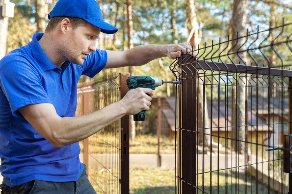 A Man Is Installing A Fence With A Drill — Rabbo's Fencing Services In Pinelands, NT