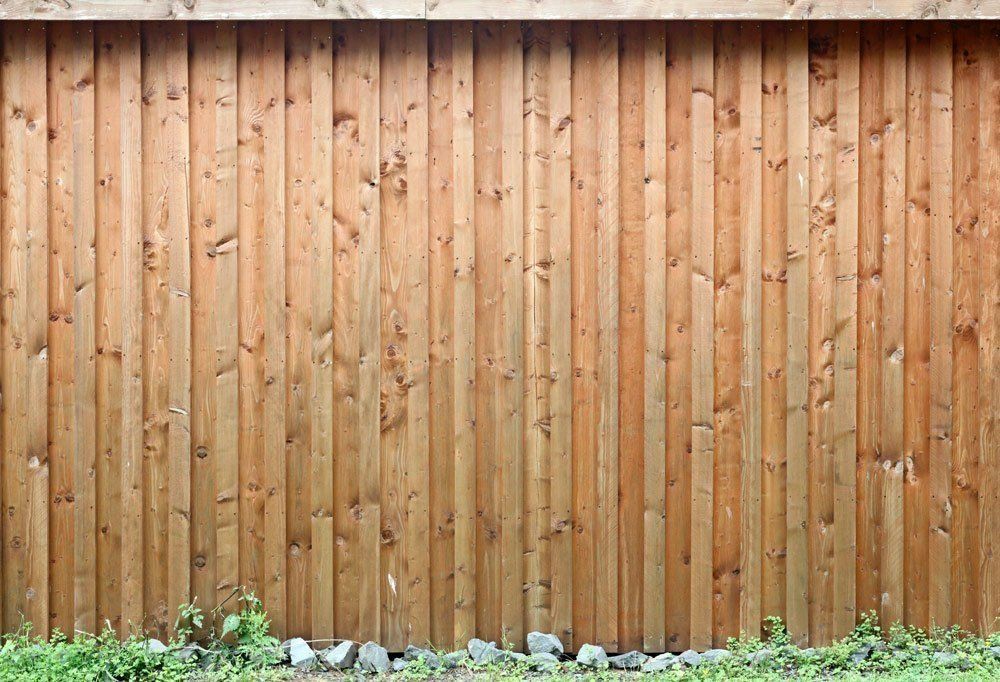 A Wooden Fence Is Surrounded By Grass And Rocks — Rabbo's Fencing Services In Pinelands, NT