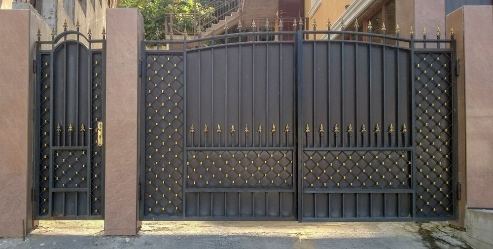 A Wrought Iron Gate Is Surrounded By Stone Pillars — Rabbo's Fencing Services In Pinelands, NT