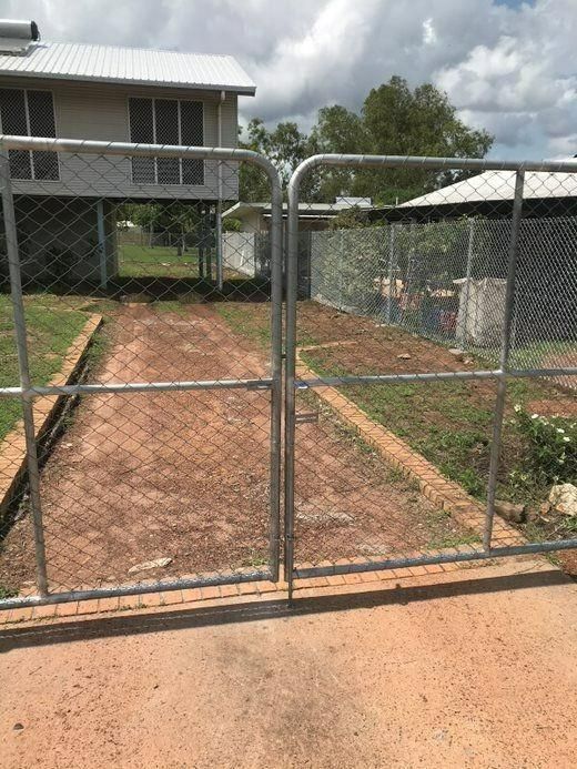 A Chain Link Fence Surrounds A Dirt Road Leading To A House — Rabbo's Fencing Services In Pinelands, NT