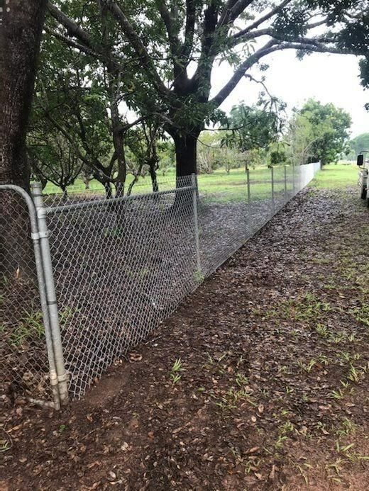 A Chain Link Fence Is Surrounding A Dirt Path With Trees In The Background — Rabbo's Fencing Services In Pinelands, NT