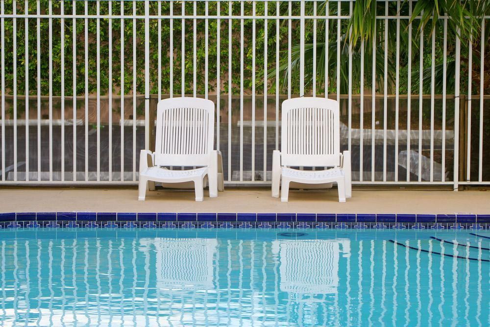 A White Pool Fence Around A Darwin Pool with White Chairs — Rabbo's Fencing Services In Pinelands, NT