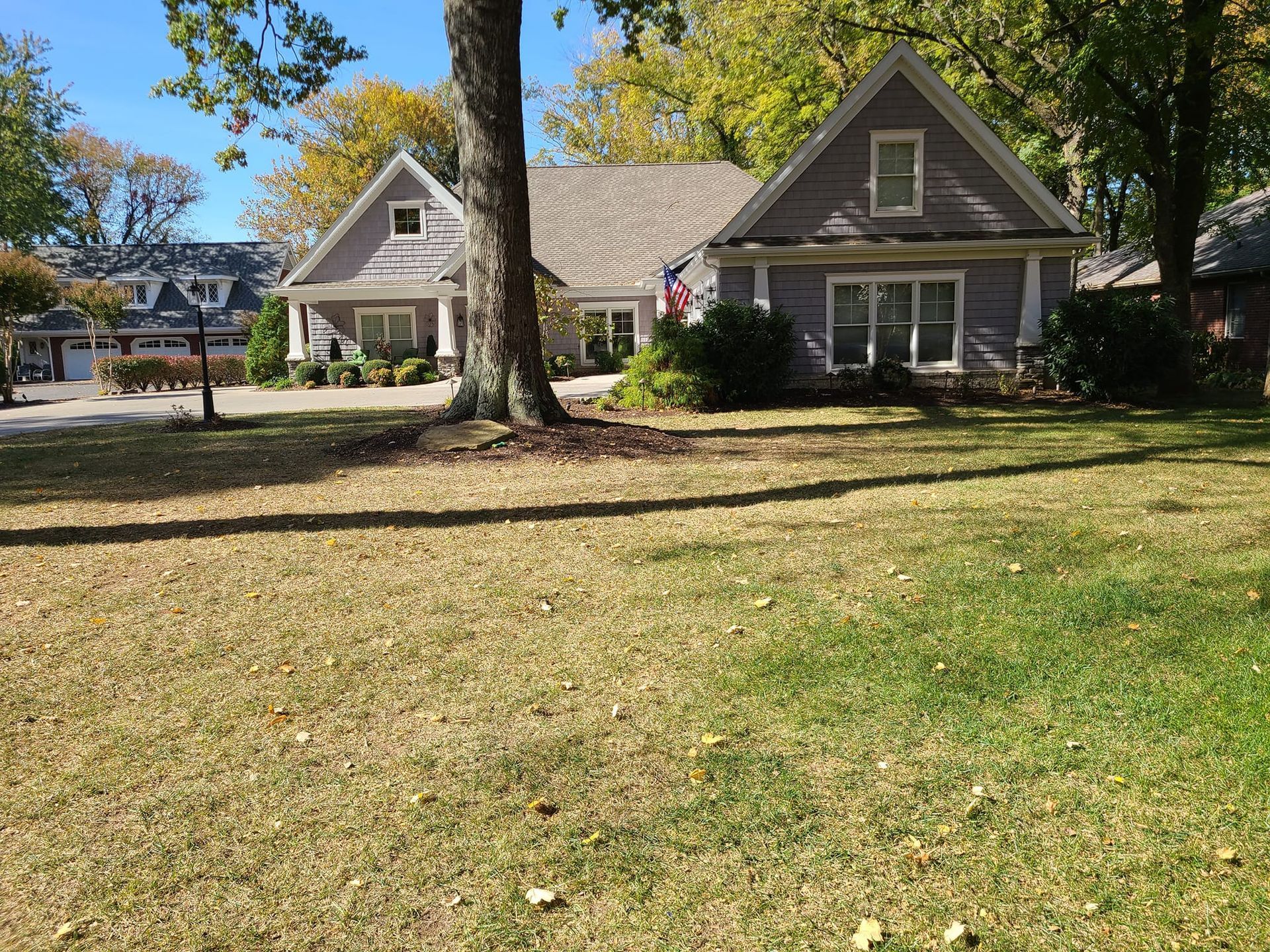 A gray house with a brown roof sits on a grassy lawn with trees in the background.