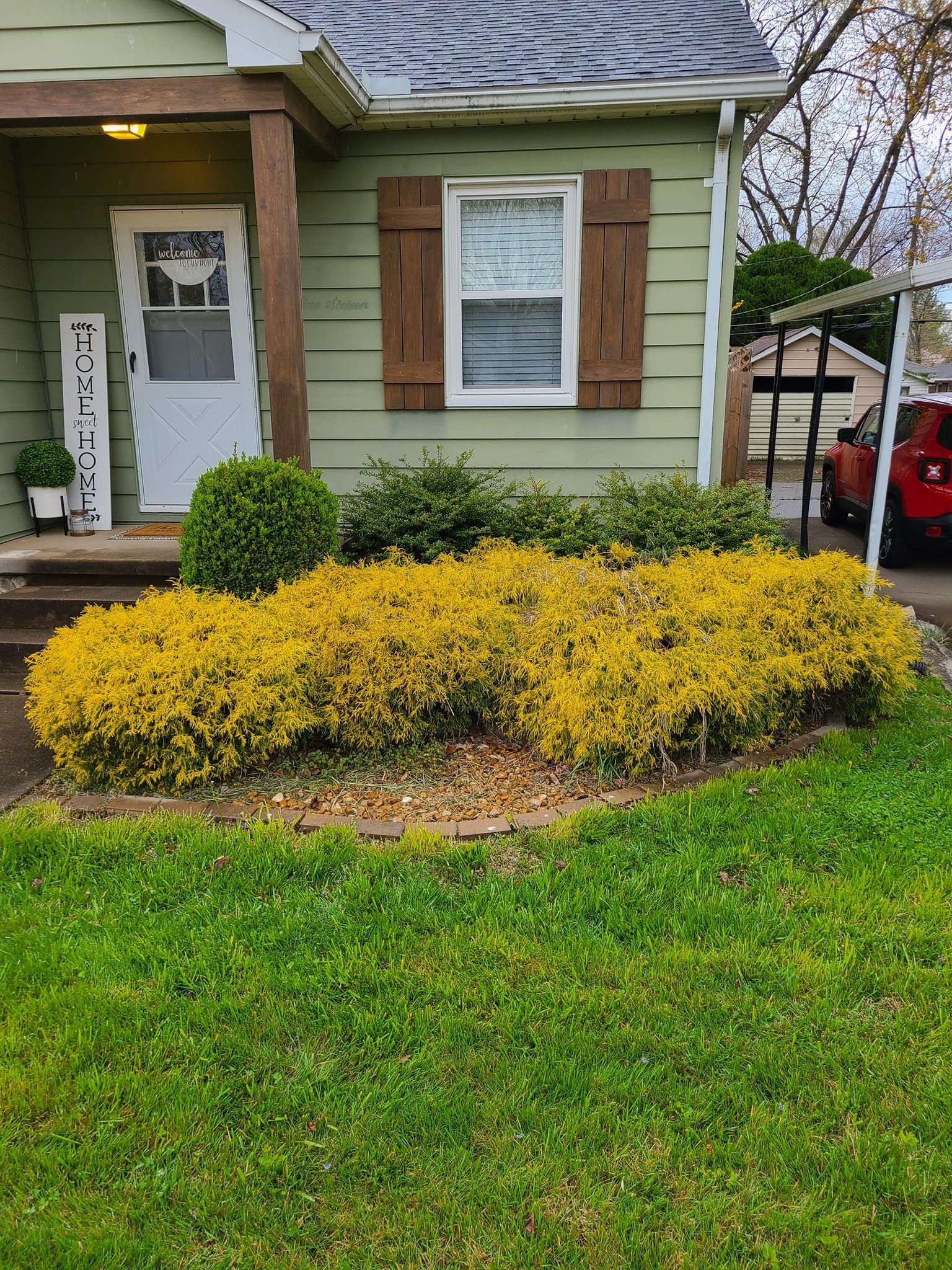 A small green house with yellow bushes in front and a sign that says 