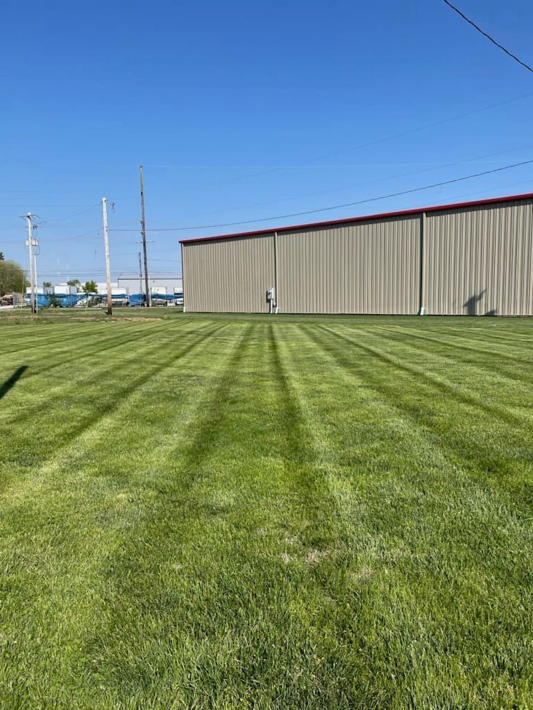 Green lawn with mower stripes in front of a tan industrial building under a blue sky.