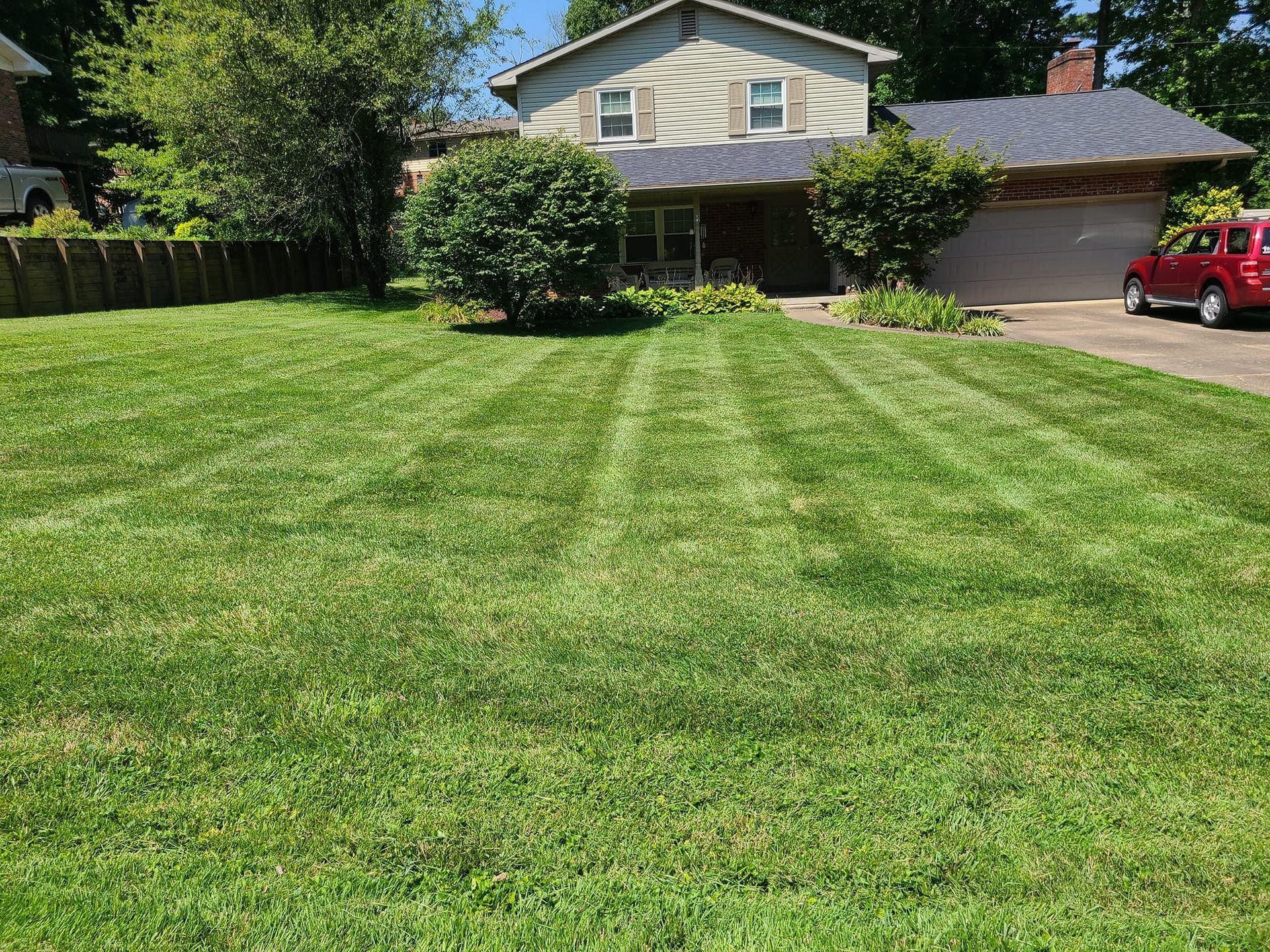 Green lawn in front of a two-story house with a striped mowing pattern on a sunny day.