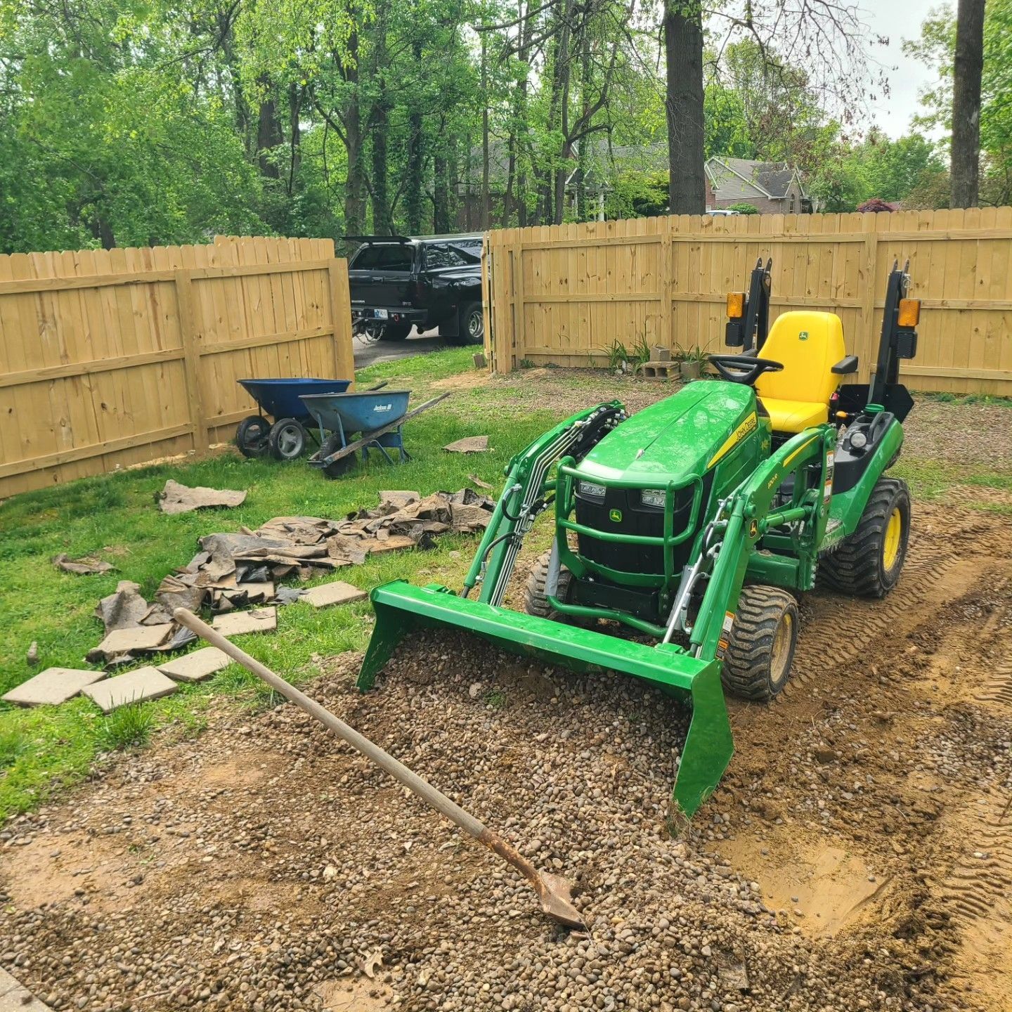 John Deere tractor with a full bucket of gravel in a yard.