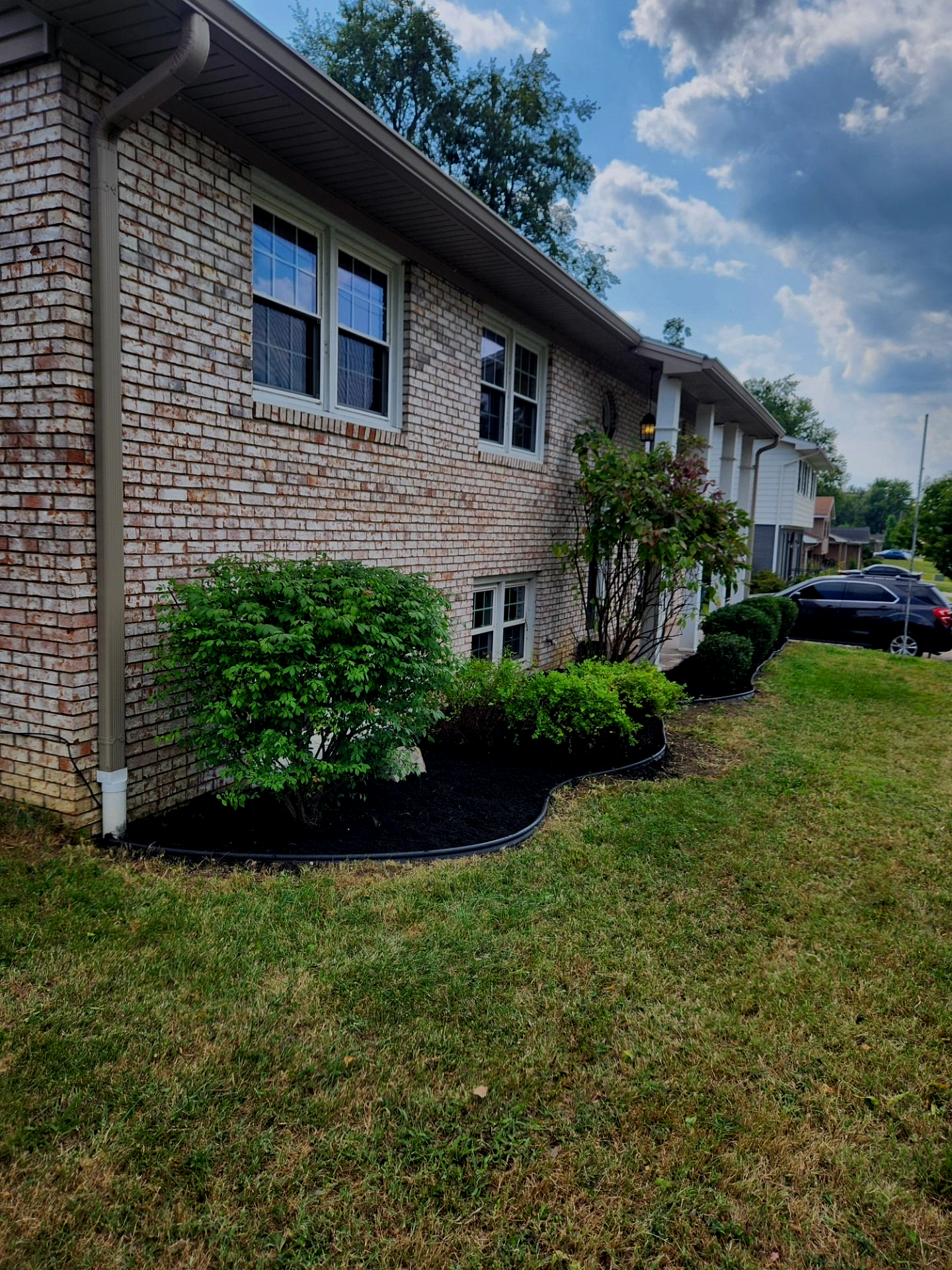 Brick apartment building with green landscaping and a cloudy sky.