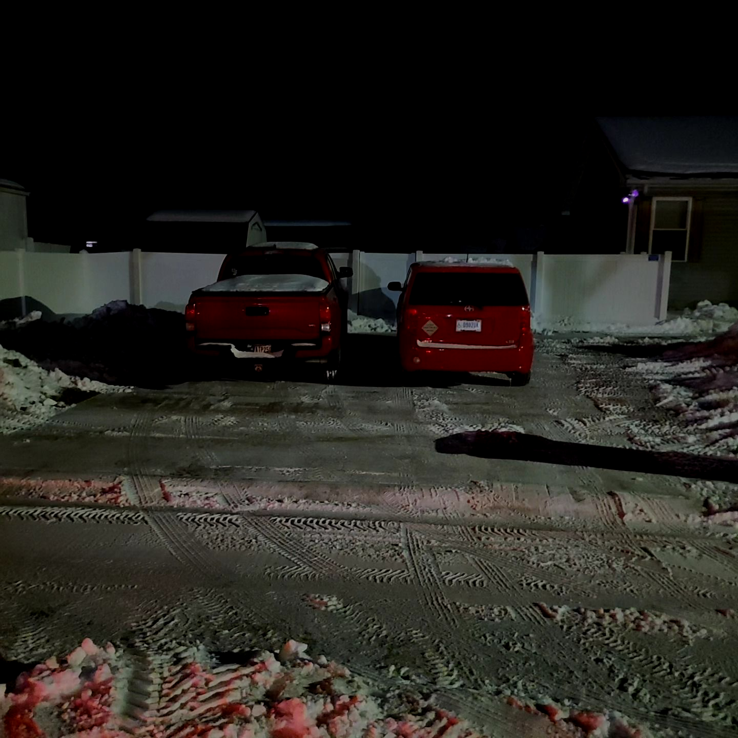 Two red vehicles parked in a snowy driveway at night, a pickup truck and a minivan.