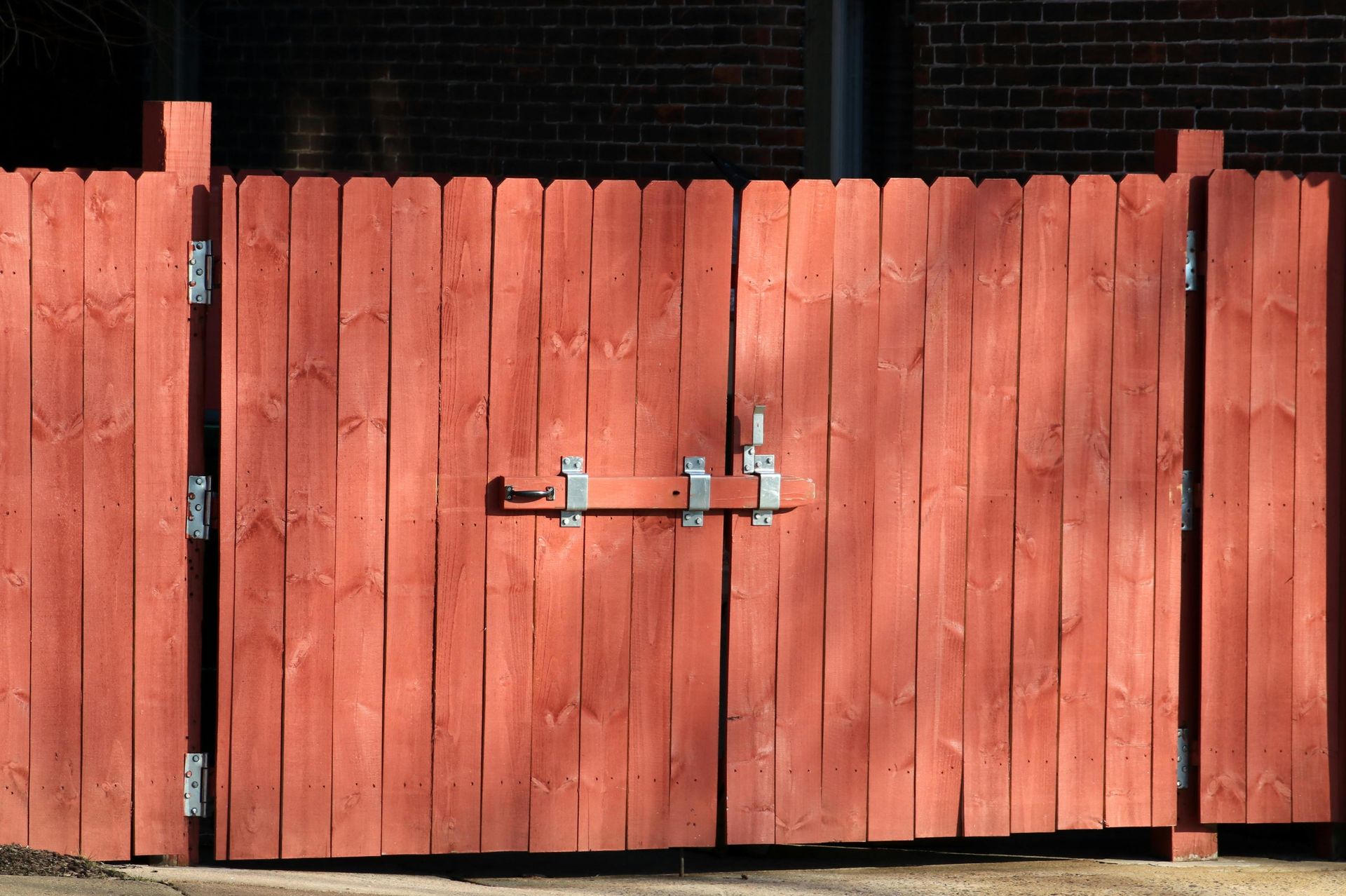 Red wooden gate with a metal latch, in front of a brick wall.