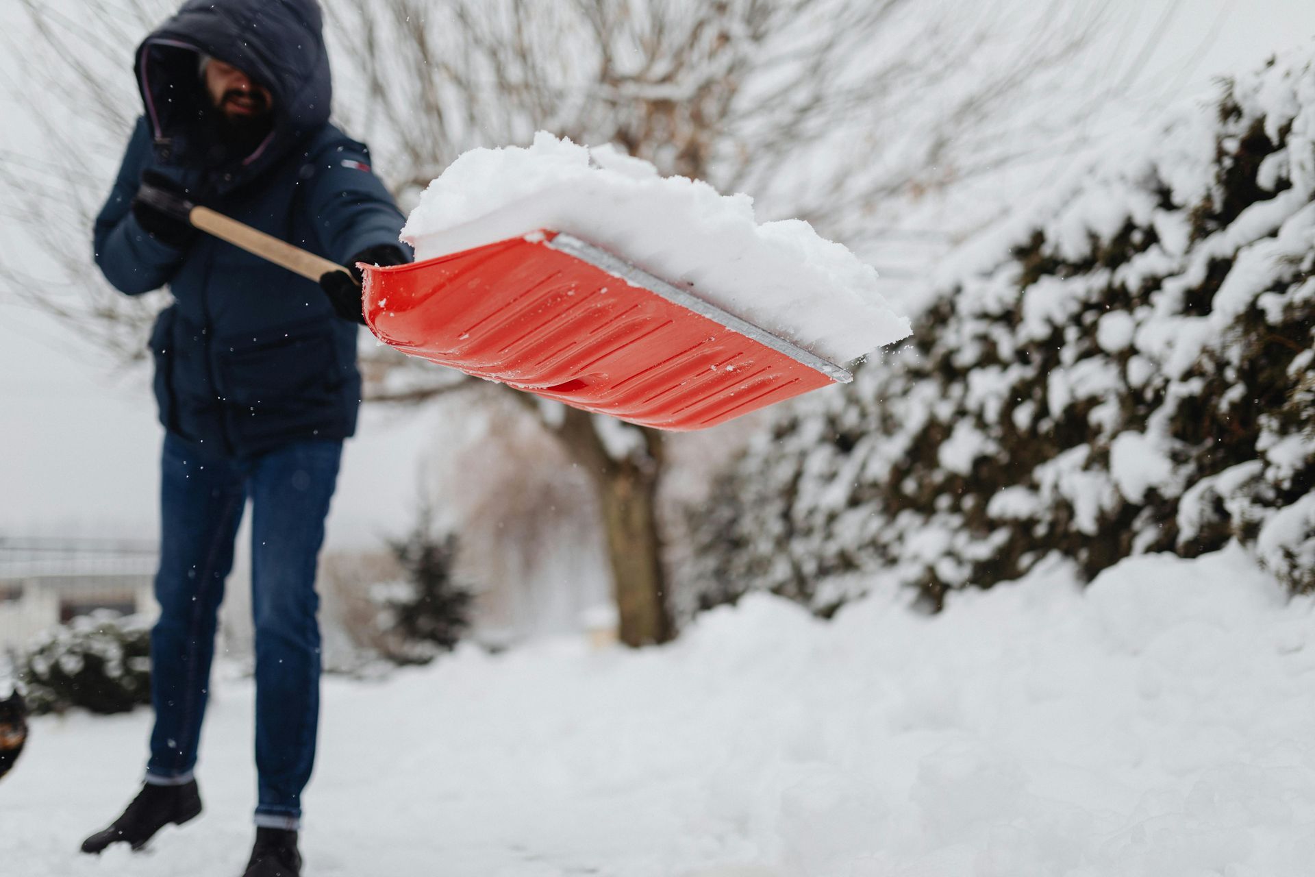 Person shoveling snow with a red shovel in a snowy yard.