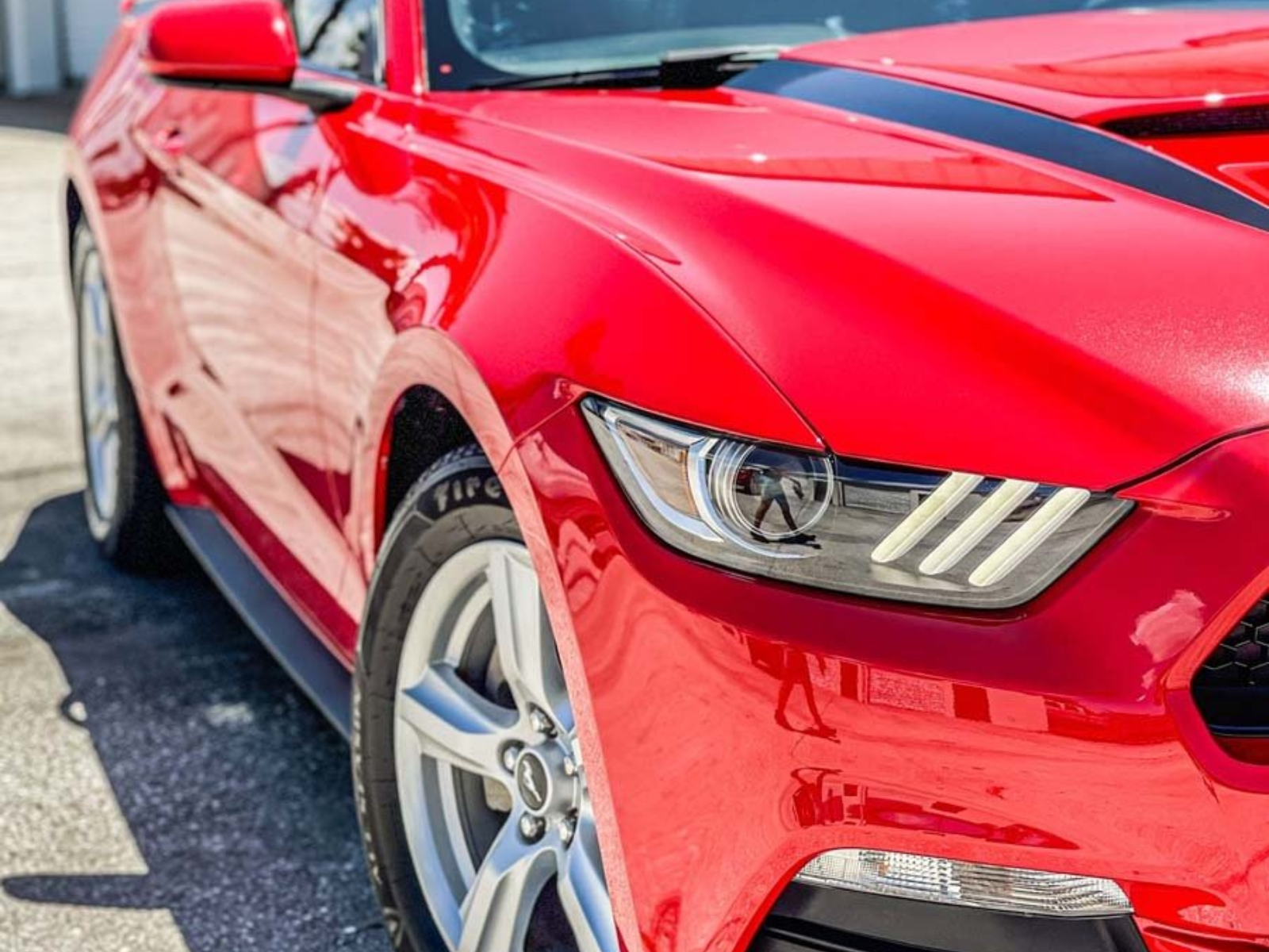 Close-up of a red sports car’s front side and headlight on a sunny street