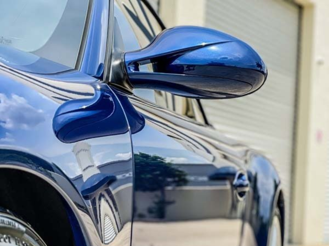 Blue sports car side mirror and door in close-up, reflecting the surroundings.