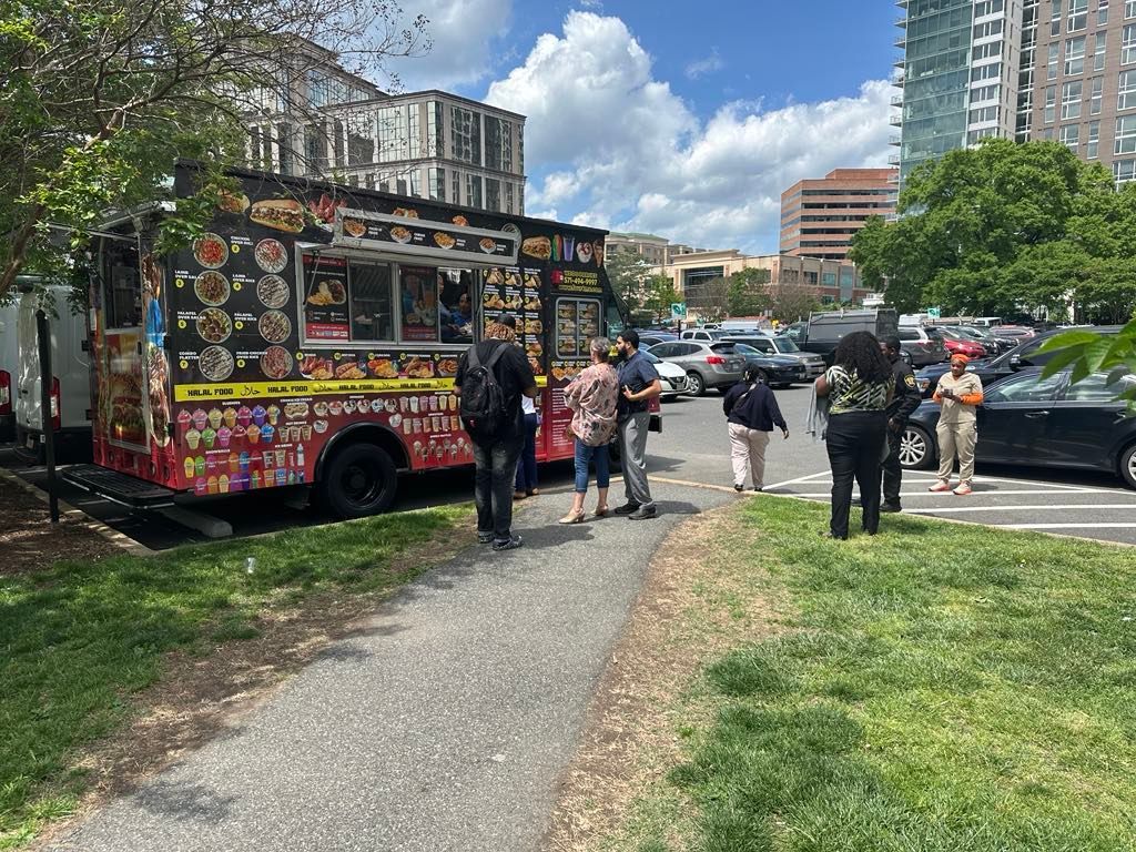A group of people are standing in front of a food truck in a parking lot.