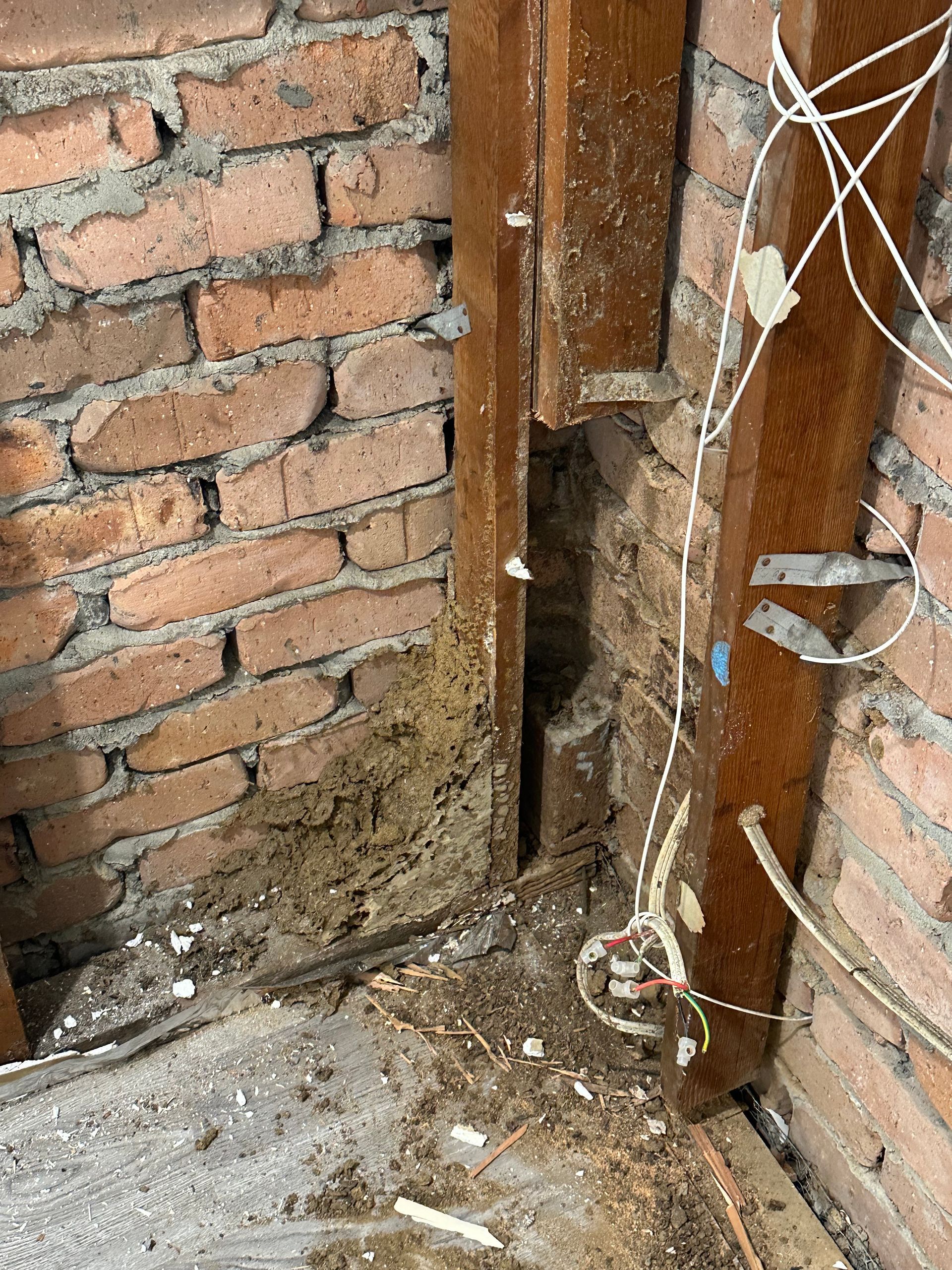 Interior view of a corner where brick walls meet a wood frame post with visible structural damage and debris.