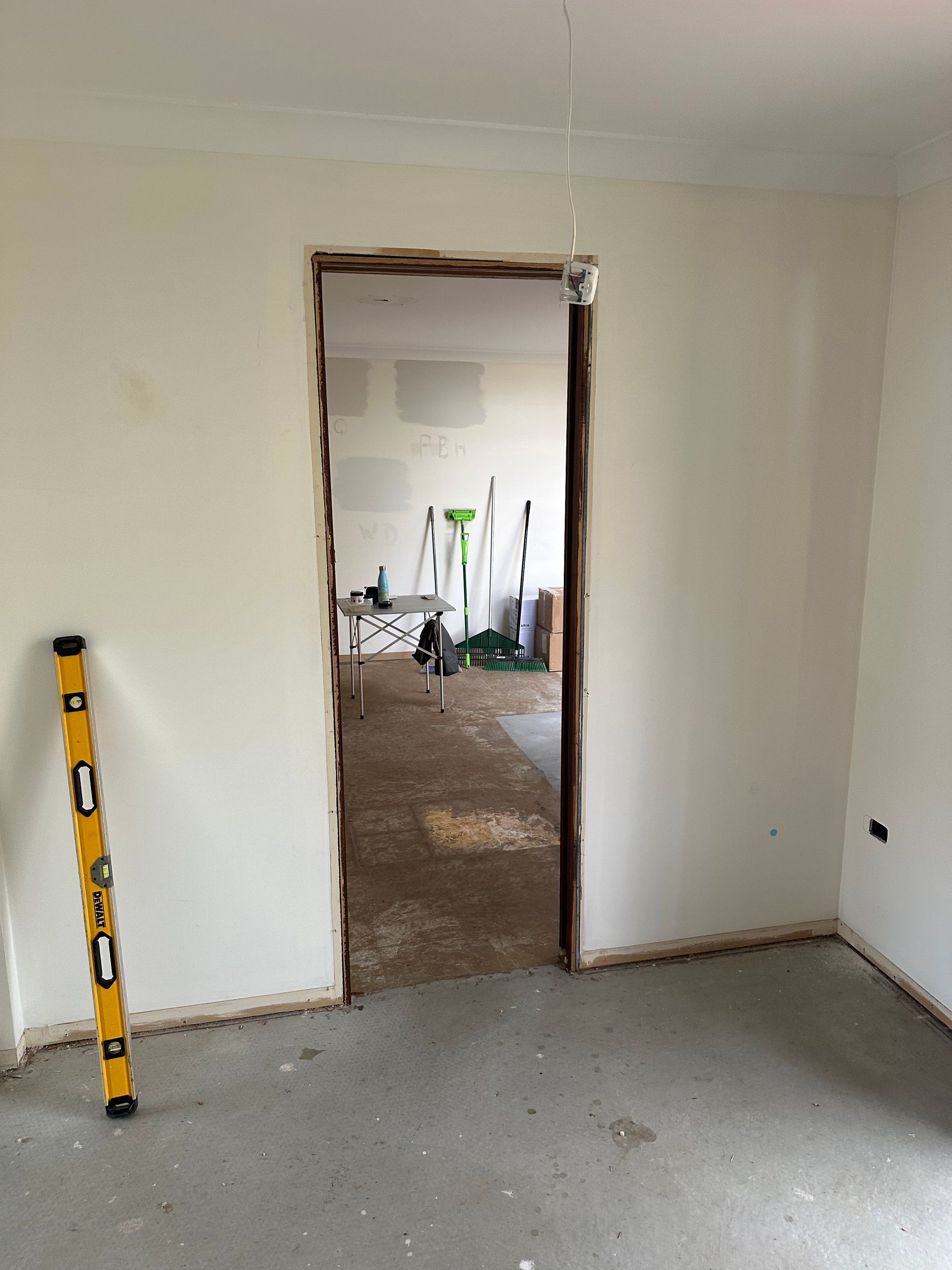 Partially finished room with white walls, bare floor, open doorway, and a yellow level leaning on the left wall