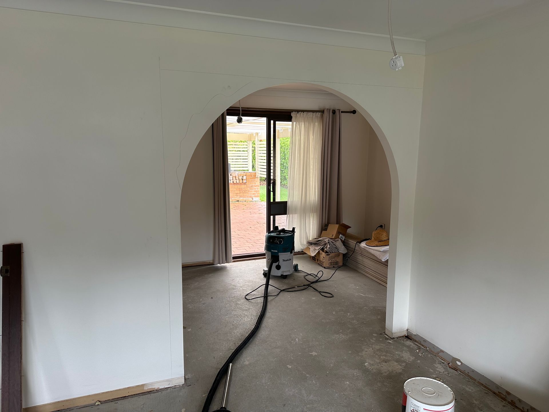 Bare room under renovation with arched doorway, tools, debris, and a hose on the floor.
