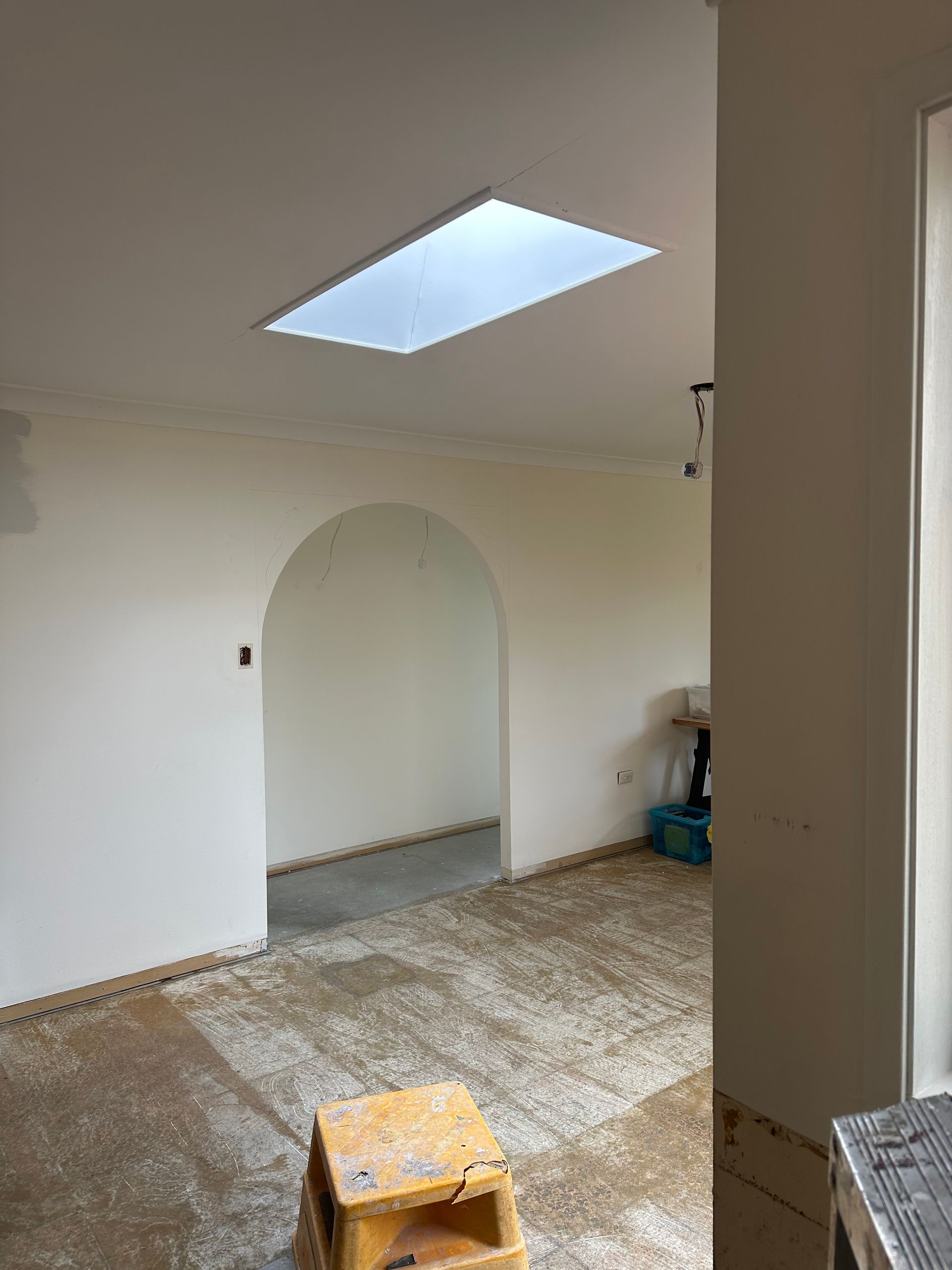 Empty room with arched doorway, skylight, and a small stool on a worn floor