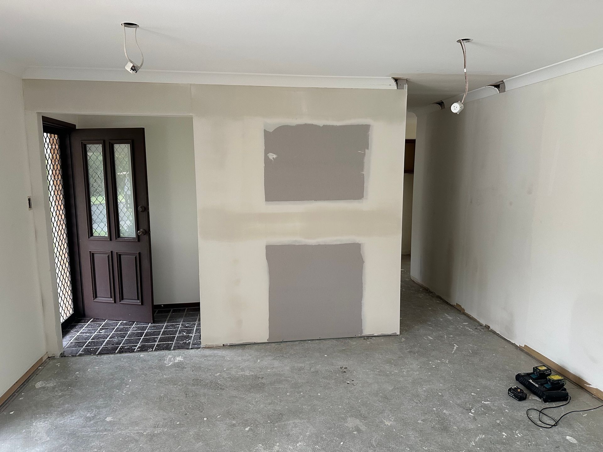 Empty room with unfinished drywall patches, white walls, gray floor, and a dark front door.
